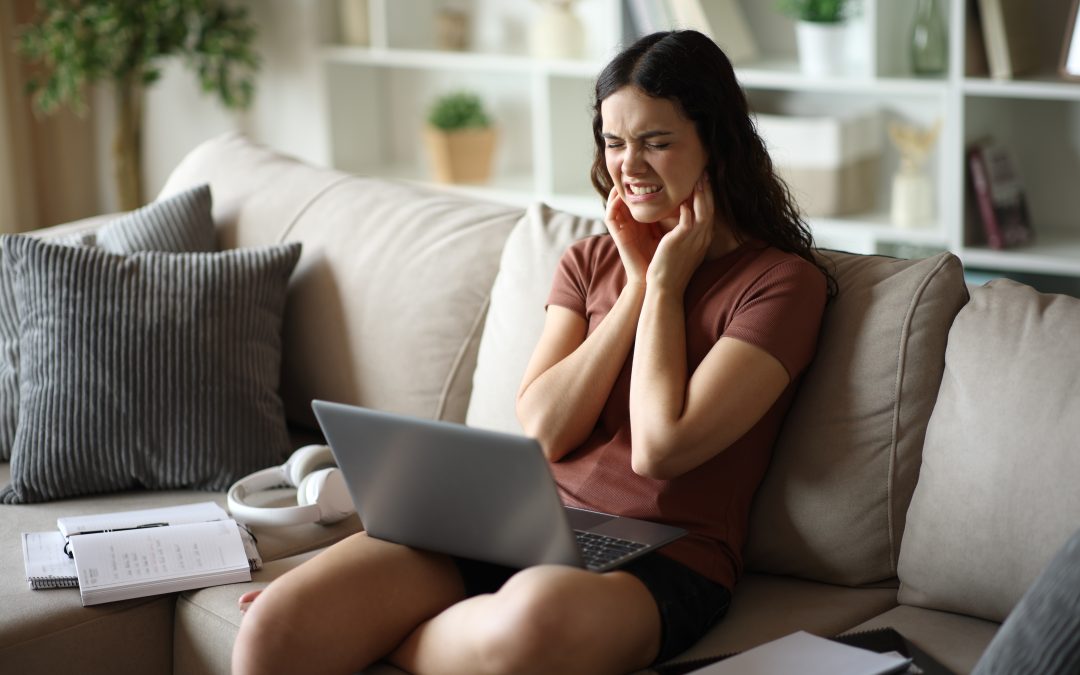 young woman sitting on a couch holding her jaw, tooth pain