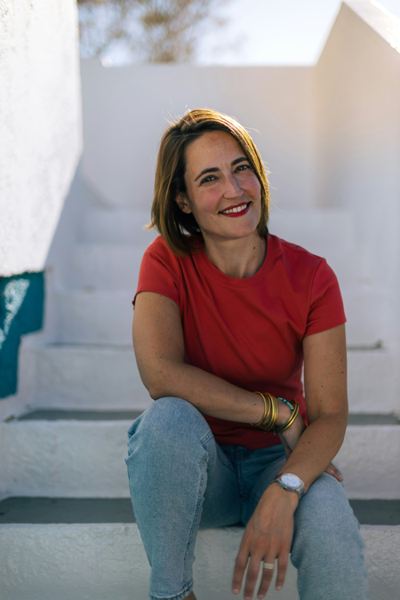 Dental implants patient sits on stairs outside in a red shirt happy with her results