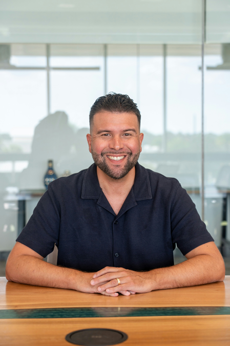 Male dental implants employee sits at a table posing for a photo with his new teeth in Florence, KY